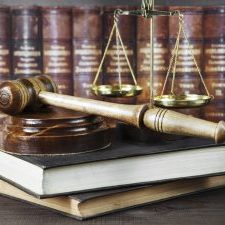 Wood gavel, soundblock, scales and stack of old books against the background of a row of antique books bound in leather